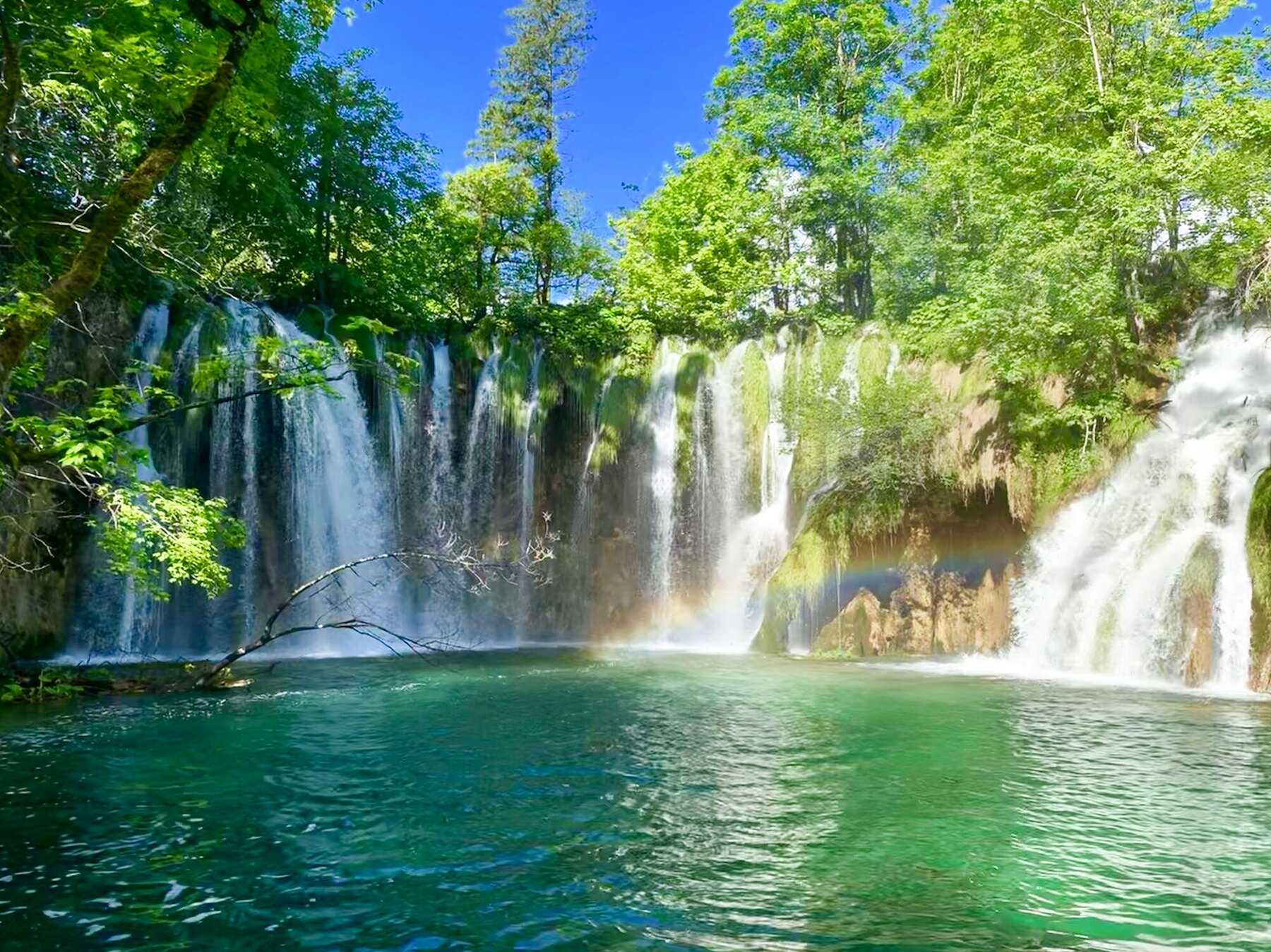Arc-en-ciel dans les embruns d'une cascade au-dessus d'un bassin turquoise, lacs de Plitvice