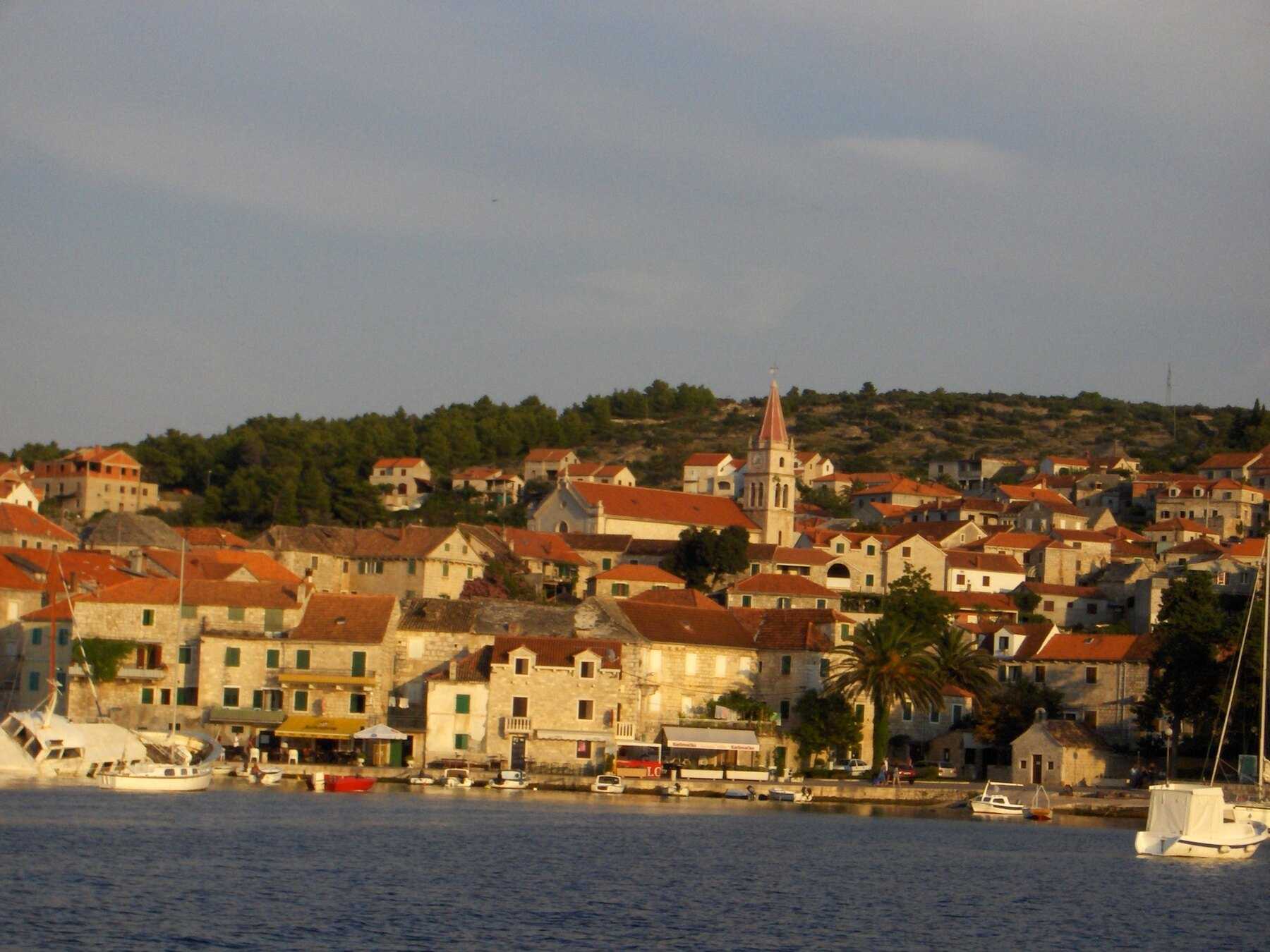 Postira et son clocher éclairés par la lumière dorée du soir, vus depuis la mer