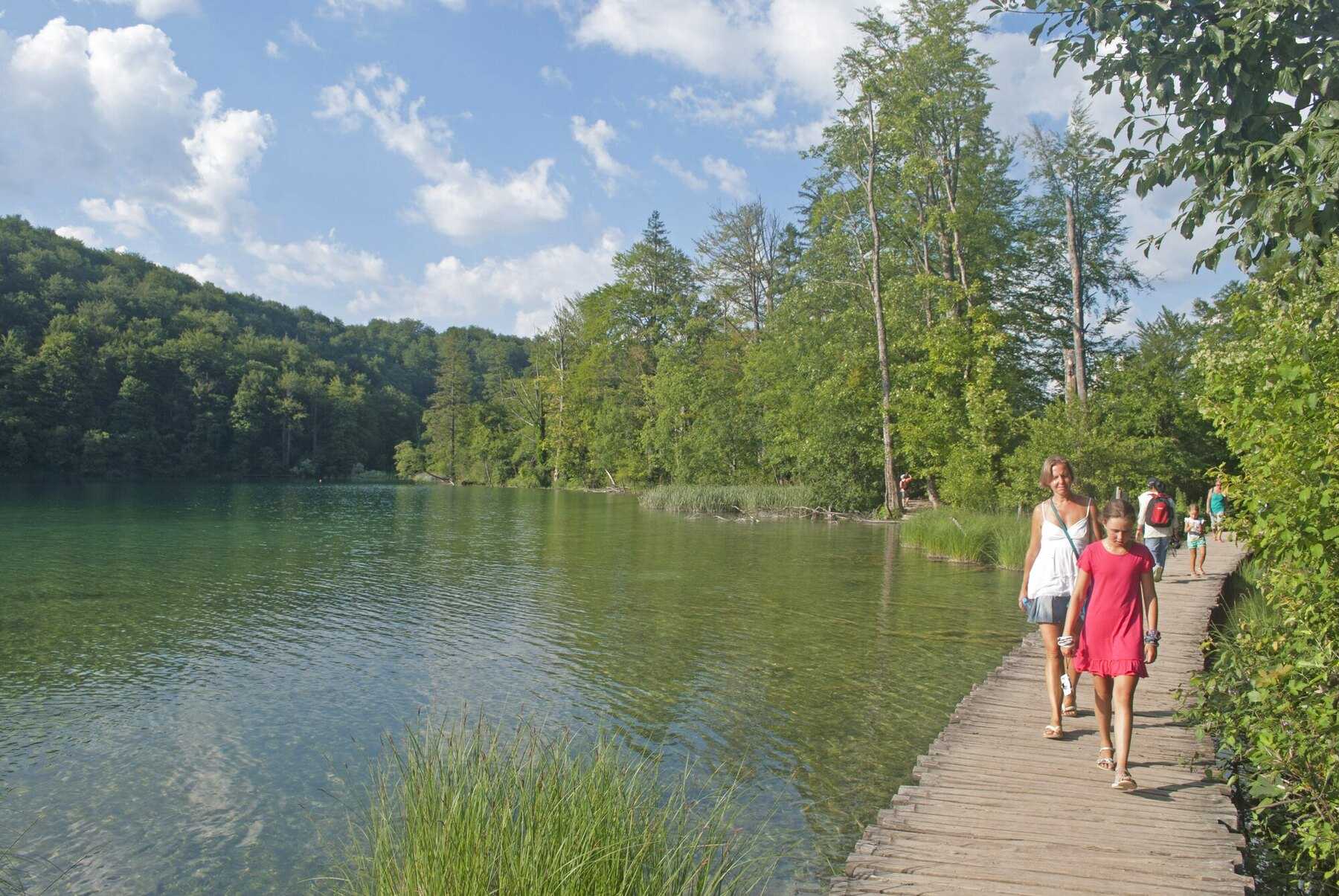 Une mère et sa fille marchent sur une passerelle en bois au bord d’un lac de Plitvice