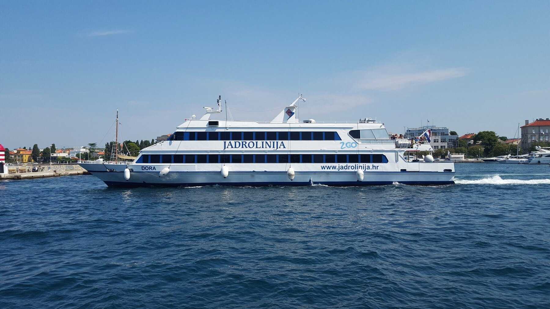 Un bateau rapide Jadrolinija, réservé aux passagers, file le long d'un quai sous un ciel bleu