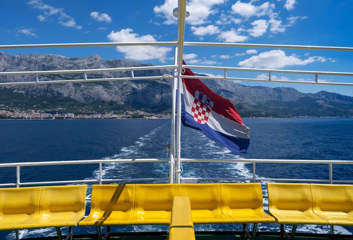 Le drapeau croate flotte à la poupe d'un car-ferry Jadrolinija, au départ de Makarska vers Sumartin, avec le massif du Biokovo en arrière-plan