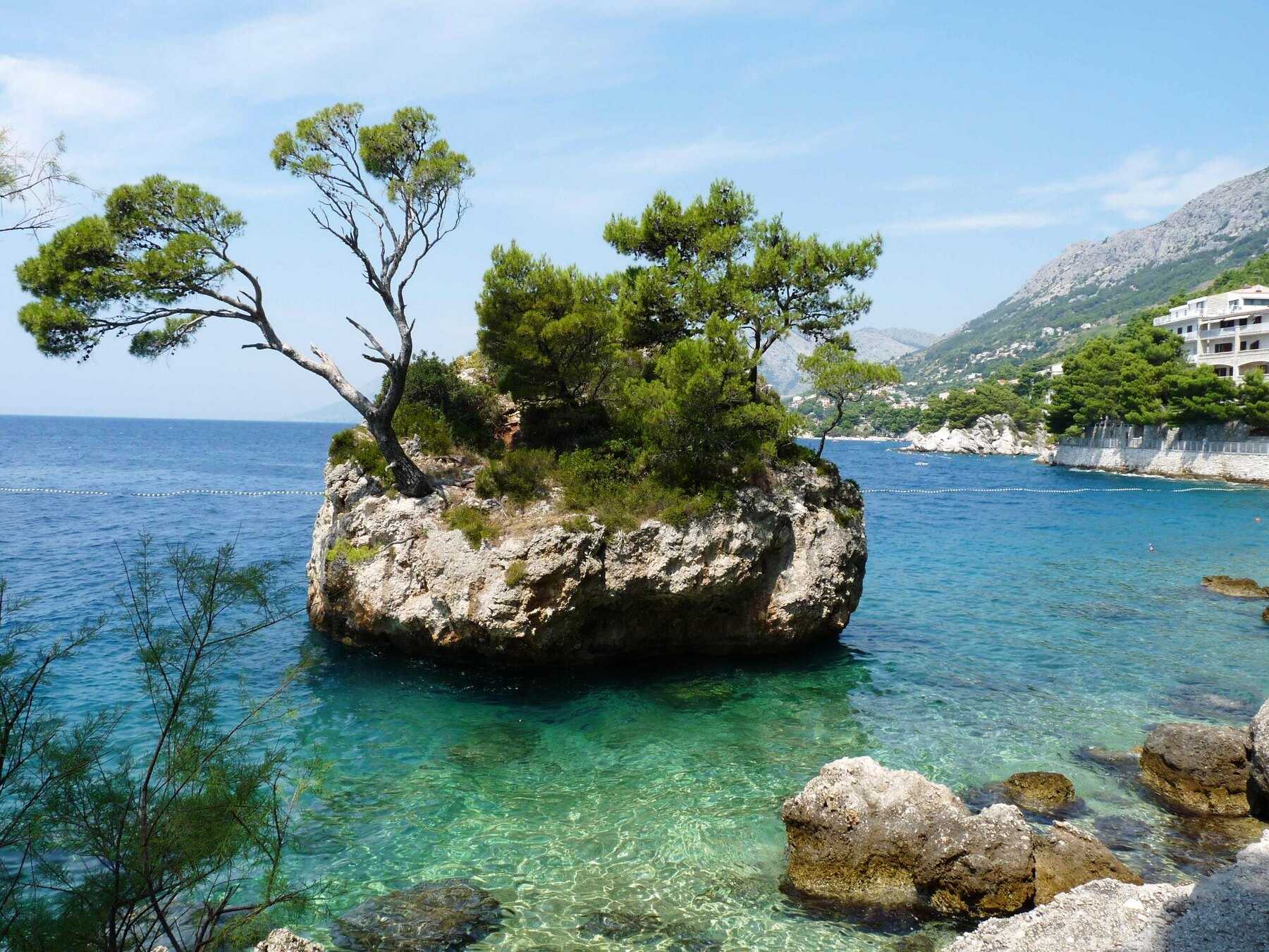 Le rocher boisé de Brela émergeant d’une eau turquoise, au pied des montagnes de la riviera de Makarska