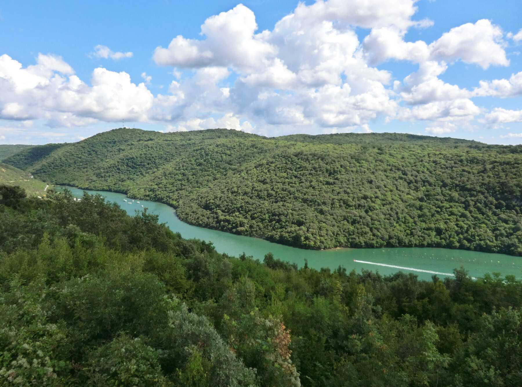 Méandre turquoise du canal de Lim entre des versants couverts de forêt