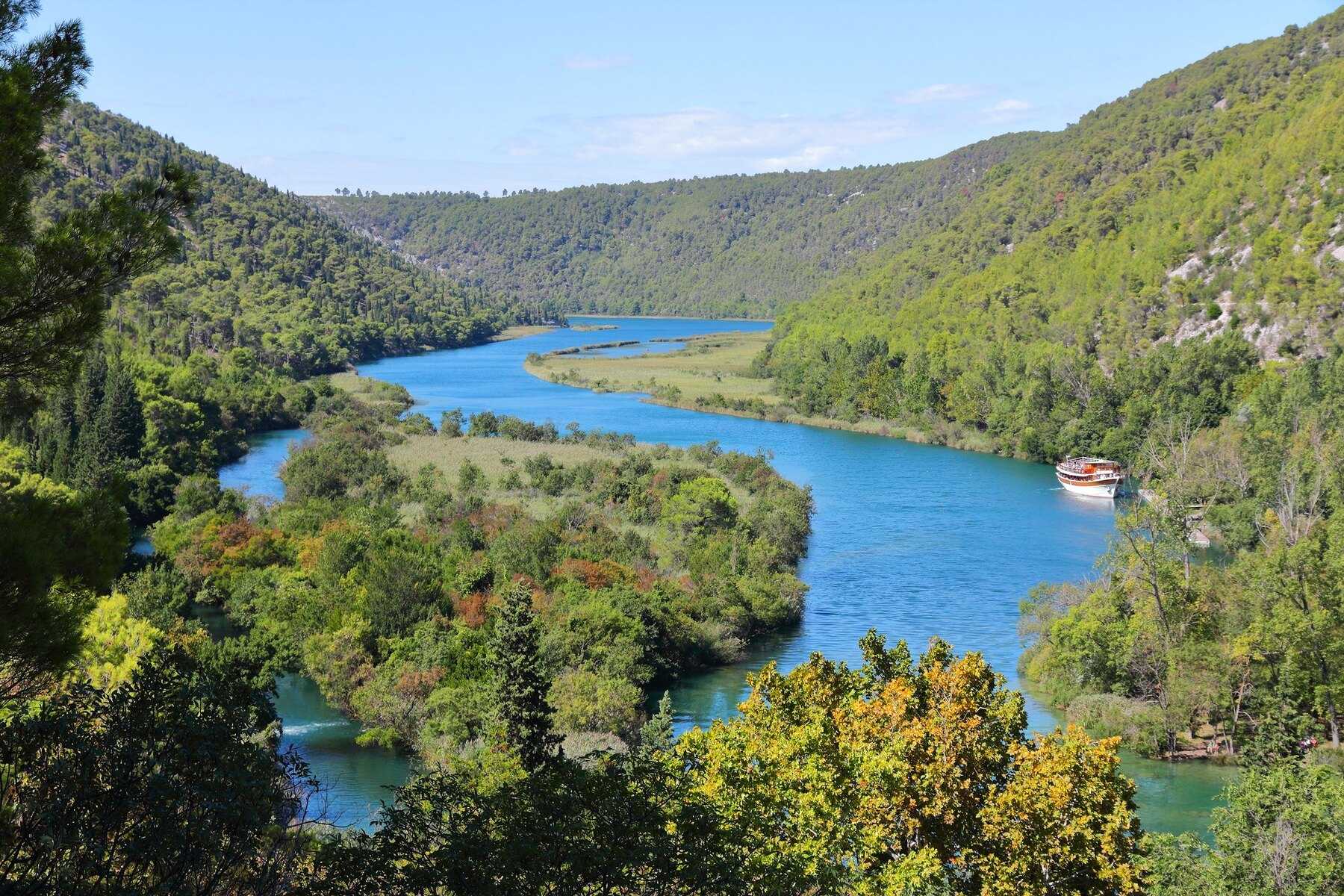 La Krka serpentant au fond de son canyon boisé, avec un bateau d'excursion