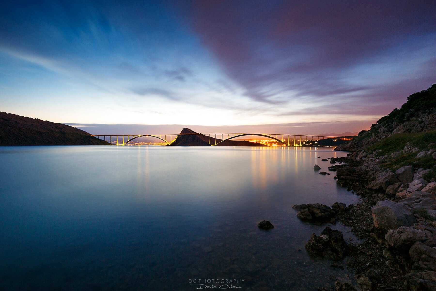 Le pont de Krk illuminé au crépuscule, au-dessus d'un bras de mer calme