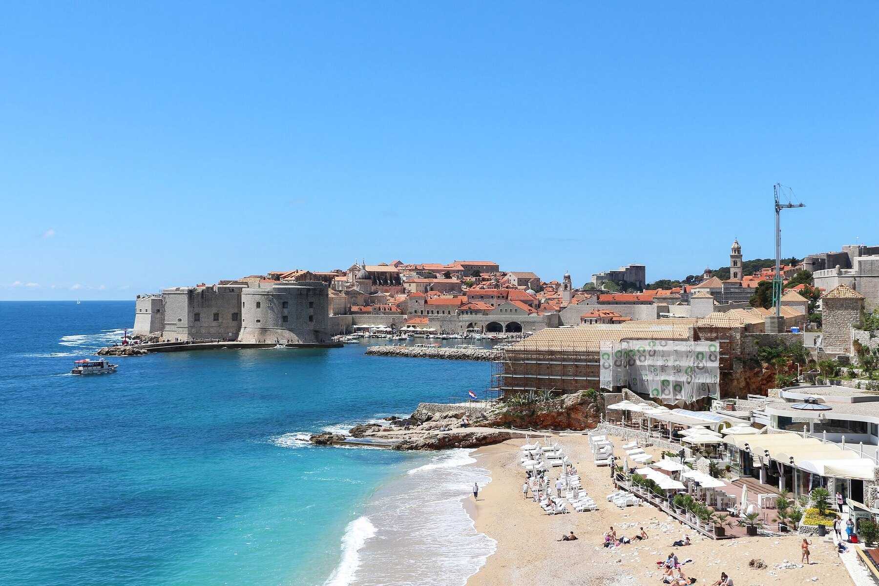 La plage de Banje et son club au premier plan, avec le fort Saint-Jean et le vieux port de Dubrovnik au fond