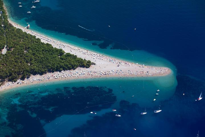 La flèche de galets de Zlatni Rat vue d’avion, bordée de pinède et d’eaux turquoise, avec des bateaux au mouillage
