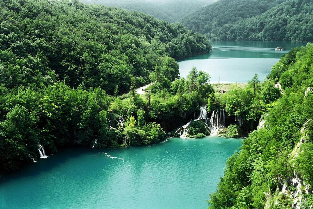 Cascades de Milanovac dévalant vers un lac turquoise, avec le lac Kozjak en arrière-plan, parc national des lacs de Plitvice