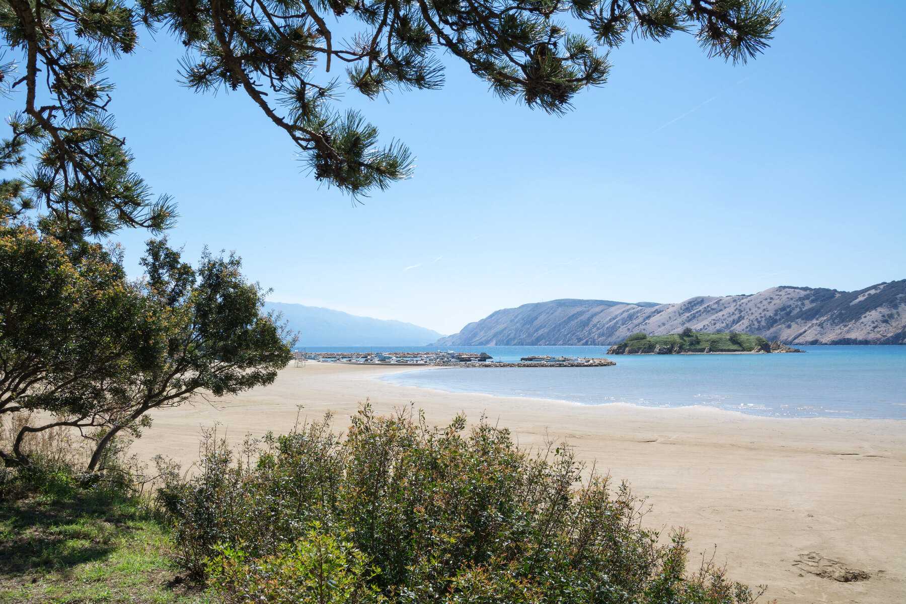 Rajska plaža à Lopar, sur l'île de Rab : une longue plage de sable clair presque déserte, sous les pins, face à un îlot
