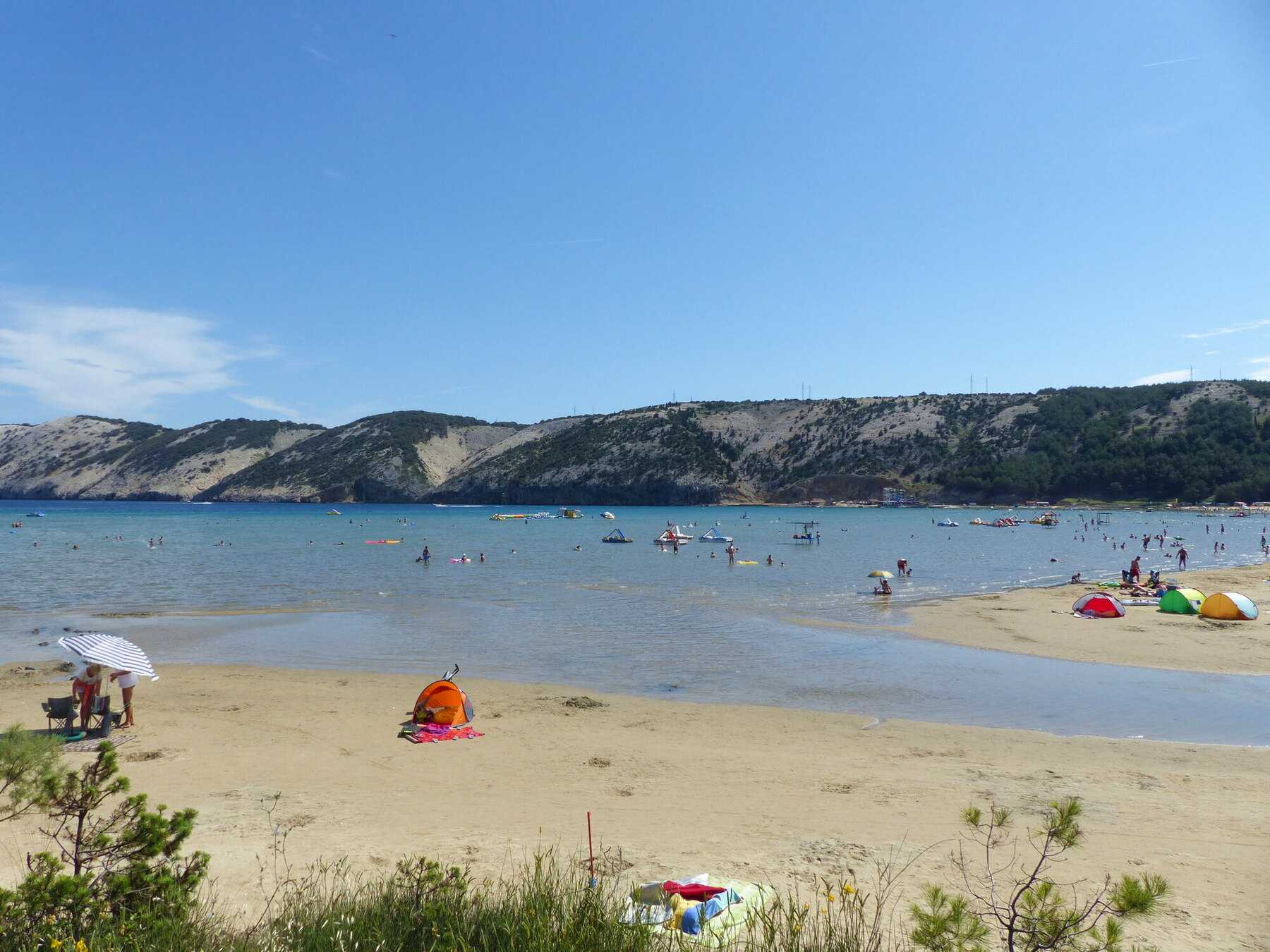Baigneurs dans l'eau peu profonde de Rajska plaža, à Lopar, en plein été, avec les collines pelées de Rab en arrière-plan