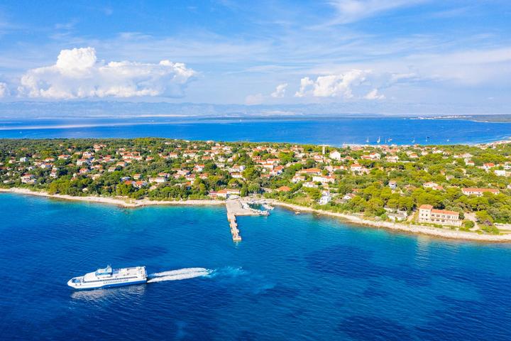 Un catamaran file sur une mer turquoise le long d'une île boisée de l'archipel de Zadar, vu du ciel
