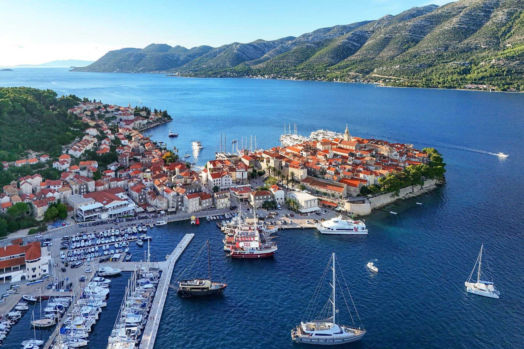 Vue aérienne de la vieille ville de Korčula sur sa presqu’île, voiliers au mouillage et montagnes de Pelješac en arrière-plan, sous le soleil de septembre