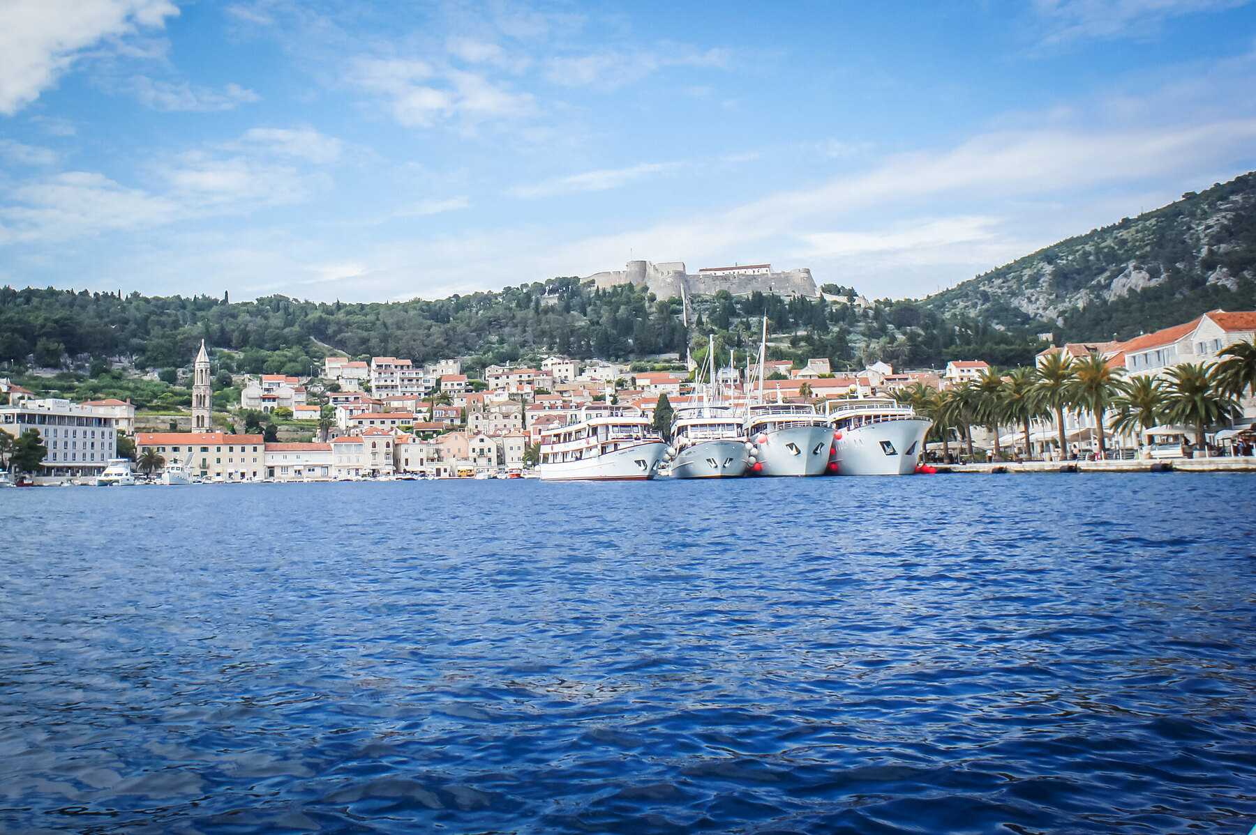 Hvar ville vue de la mer, avec la forteresse au-dessus des maisons et des bateaux le long du quai