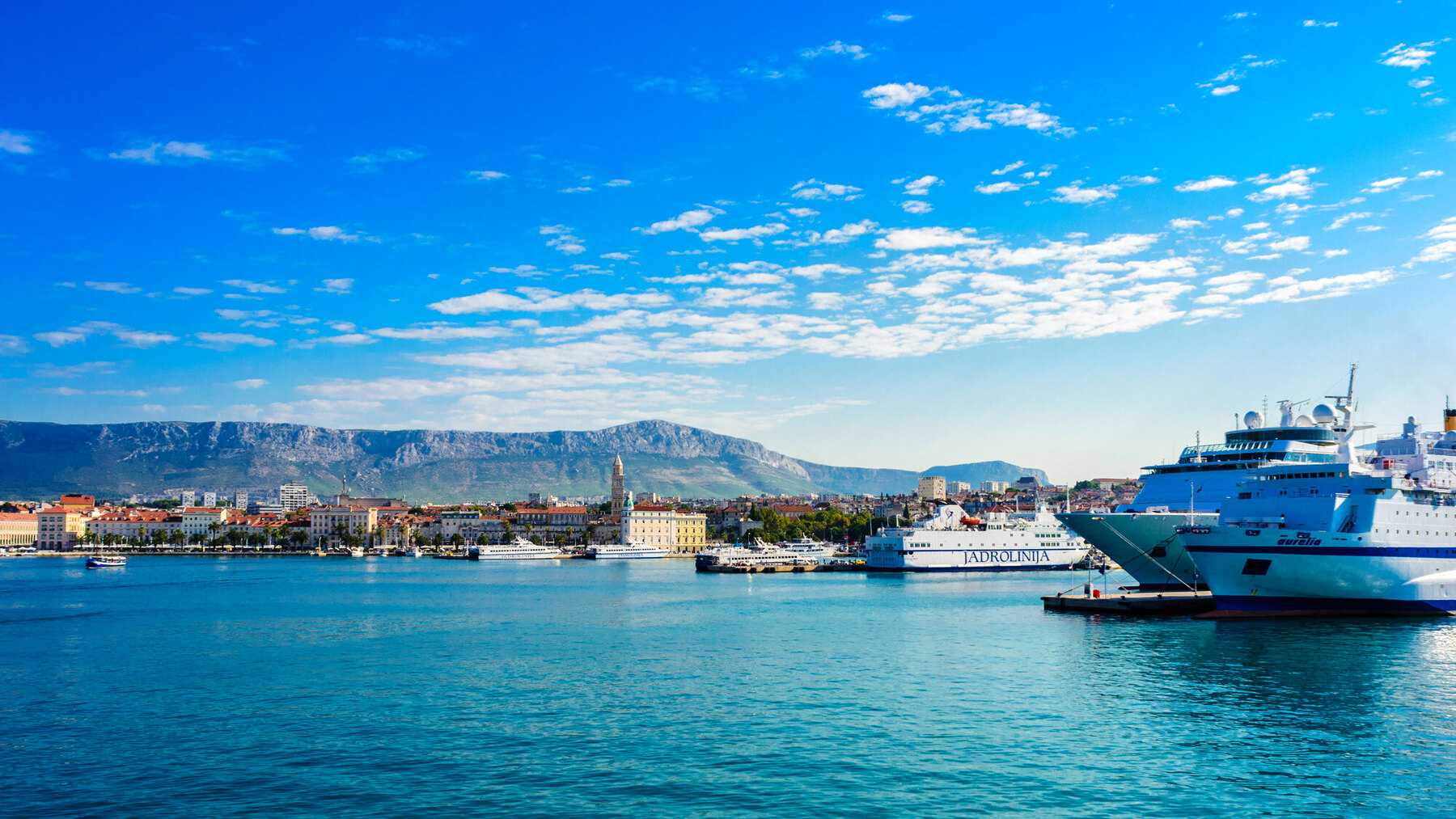 Le port de Split vu de la mer, avec ses ferries à quai, la vieille ville et les montagnes en arrière-plan