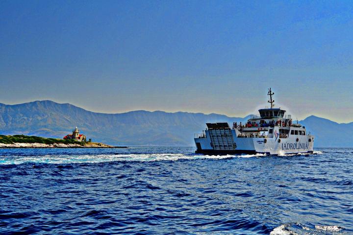 Un car-ferry Jadrolinija en pleine mer, au large d'un petit phare, avec les montagnes de la côte dalmate à l'horizon