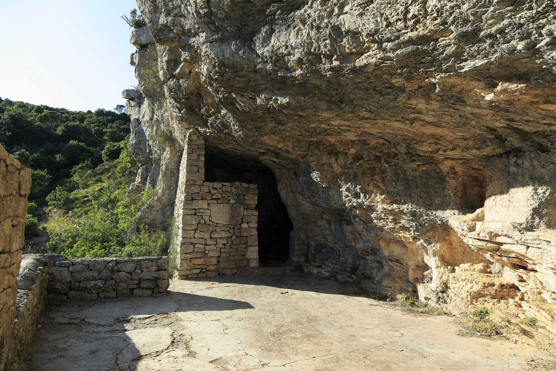 L'entrée maçonnée de la grotte de Tito sous un surplomb rocheux